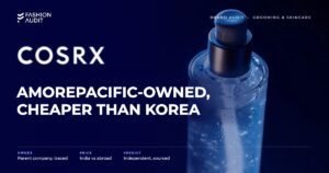 COSRX brand audit by FashionAudit: COSRX logo and the headline “Amorepacific-Owned, Cheaper Than Korea” over Korean snail mucin essence bottle with a dewy glass texture